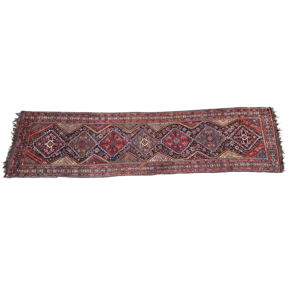 An antique Persian Shiraz wool runner rug featuring a sequence of geometric diamond medallions in crimson red and navy blue with fringed ends. View III