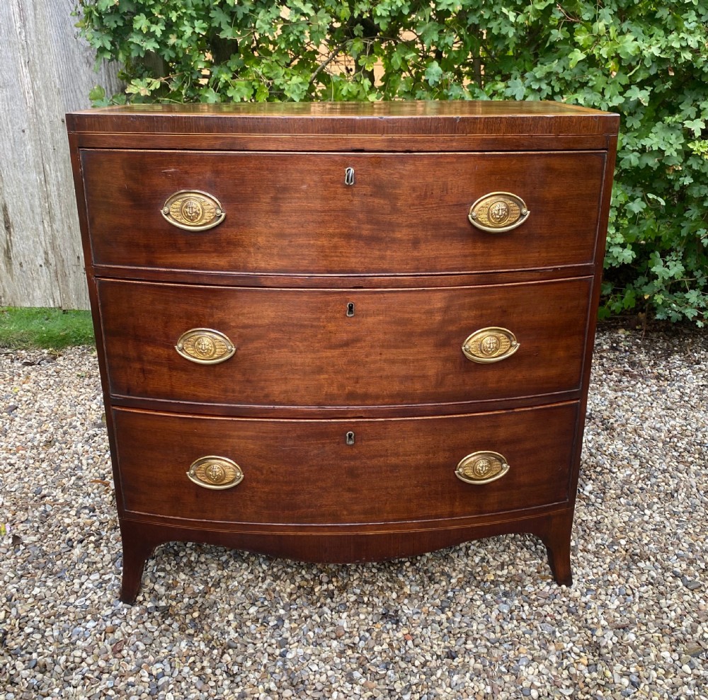 An early nineteenth-century mahogany bow-fronted chest of drawers featuring satinwood crossbanding, three graduated drawers, and oval brass handles. View II