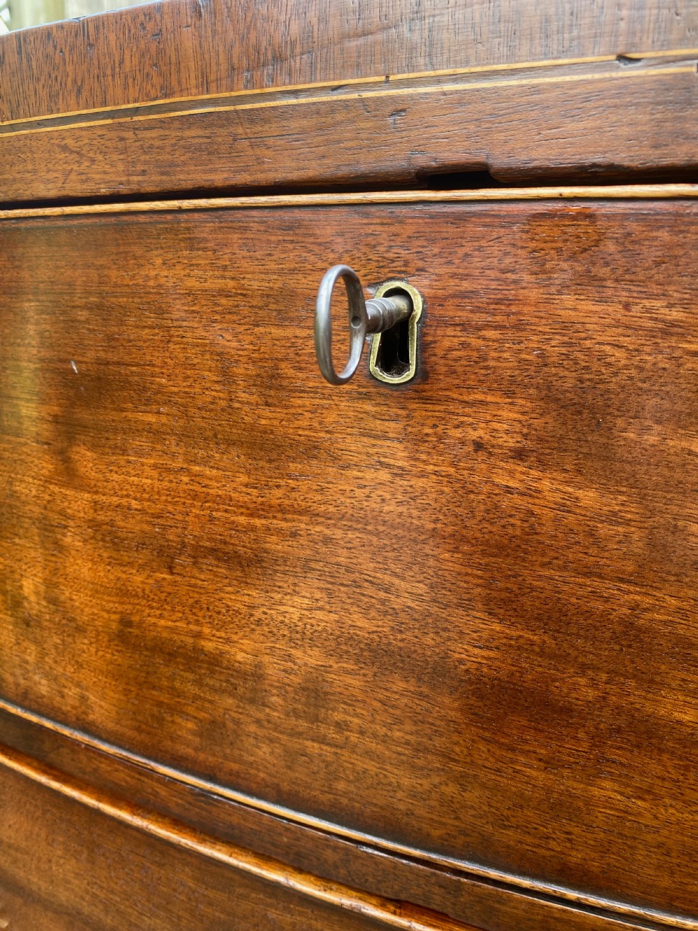 An early nineteenth-century mahogany bow-fronted chest of drawers featuring satinwood crossbanding, three graduated drawers, and oval brass handles. View III