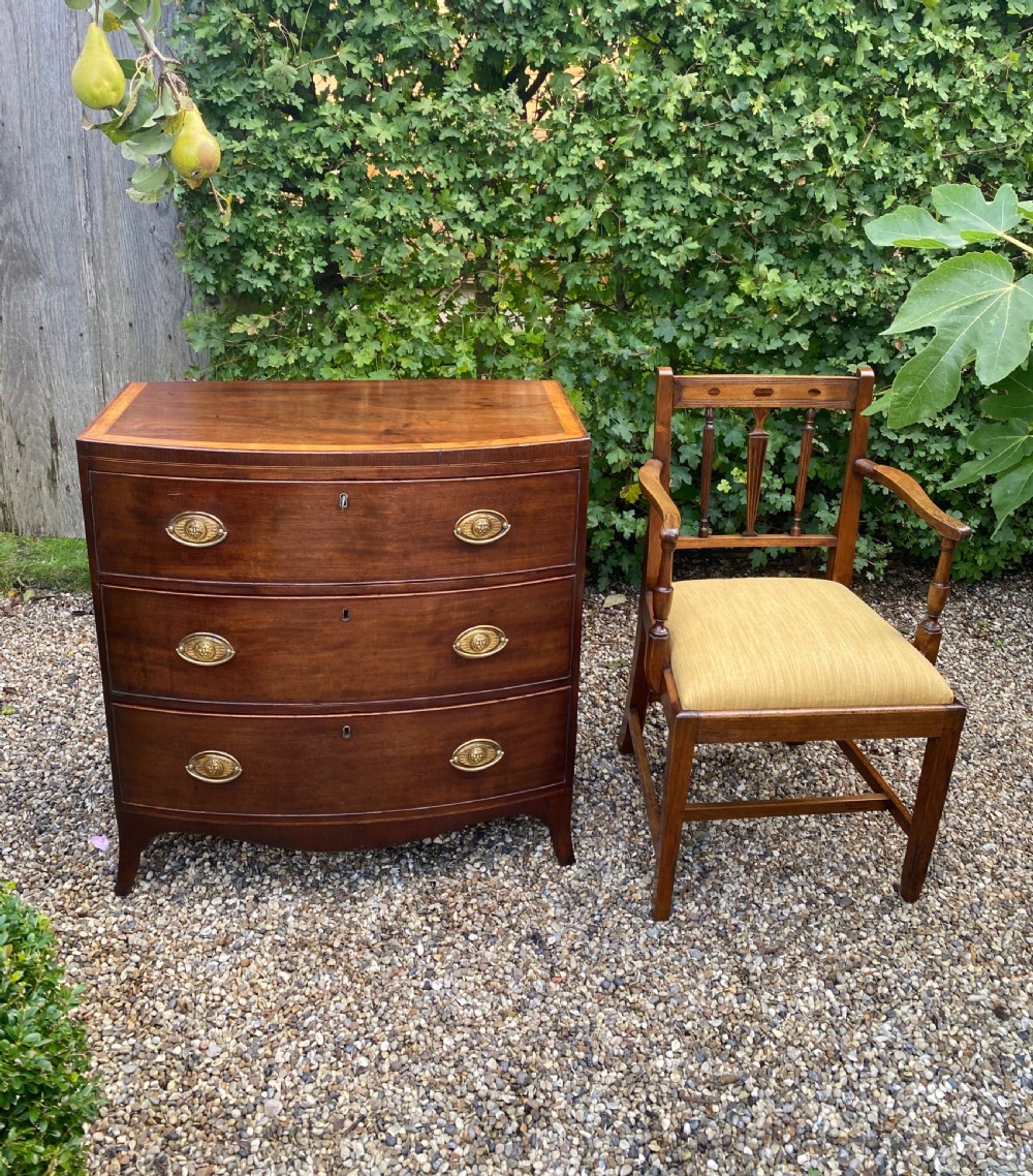 An early nineteenth-century mahogany bow-fronted chest of drawers featuring satinwood crossbanding, three graduated drawers, and oval brass handles. View IV
