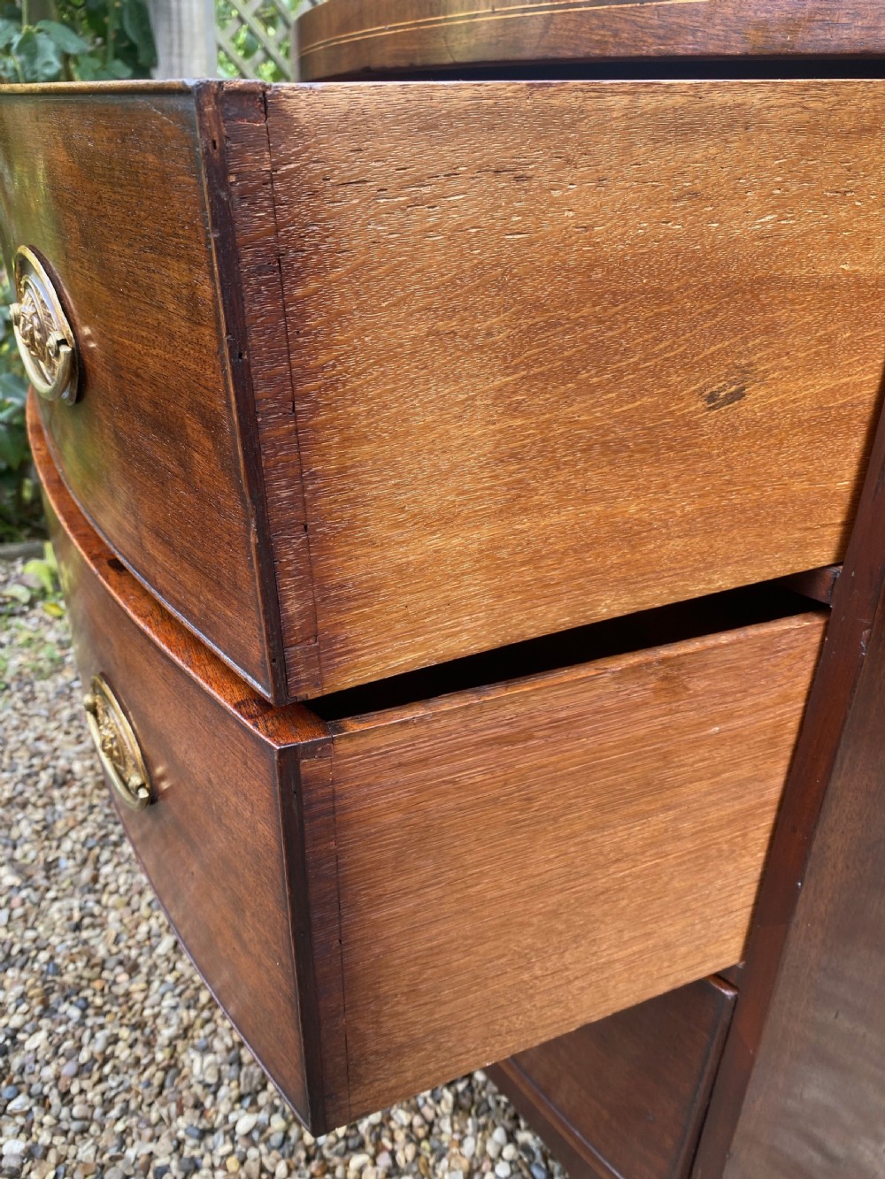 An early nineteenth-century mahogany bow-fronted chest of drawers featuring satinwood crossbanding, three graduated drawers, and oval brass handles. View VI