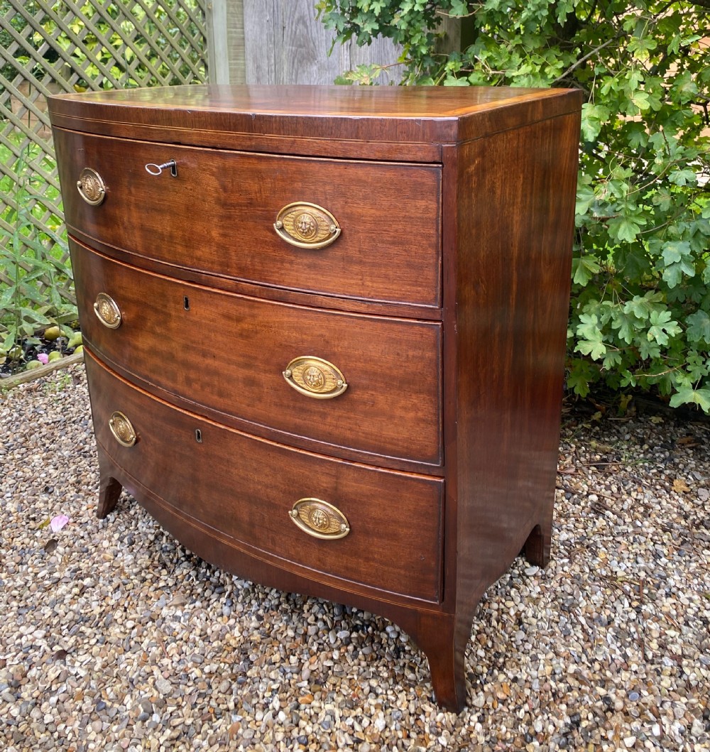 An early nineteenth-century mahogany bow-fronted chest of drawers featuring satinwood crossbanding, three graduated drawers, and oval brass handles. View VII