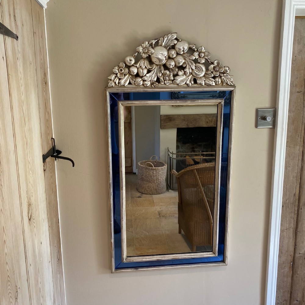 A vertical rectangular Venetian wall mirror featuring a carved silvered fruit pediment, silver gilt framing, and cobalt blue glass border panels.