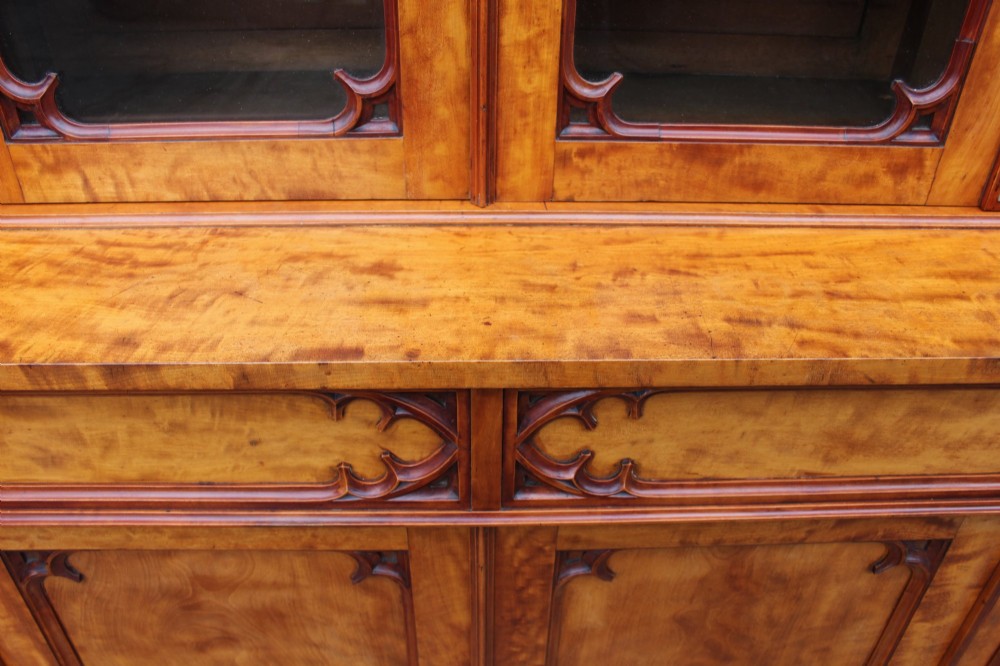 A 19th century Gothic Revival two-part satinwood bookcase featuring glazed upper doors with Gothic tracery and a matching lower cupboard section. View V