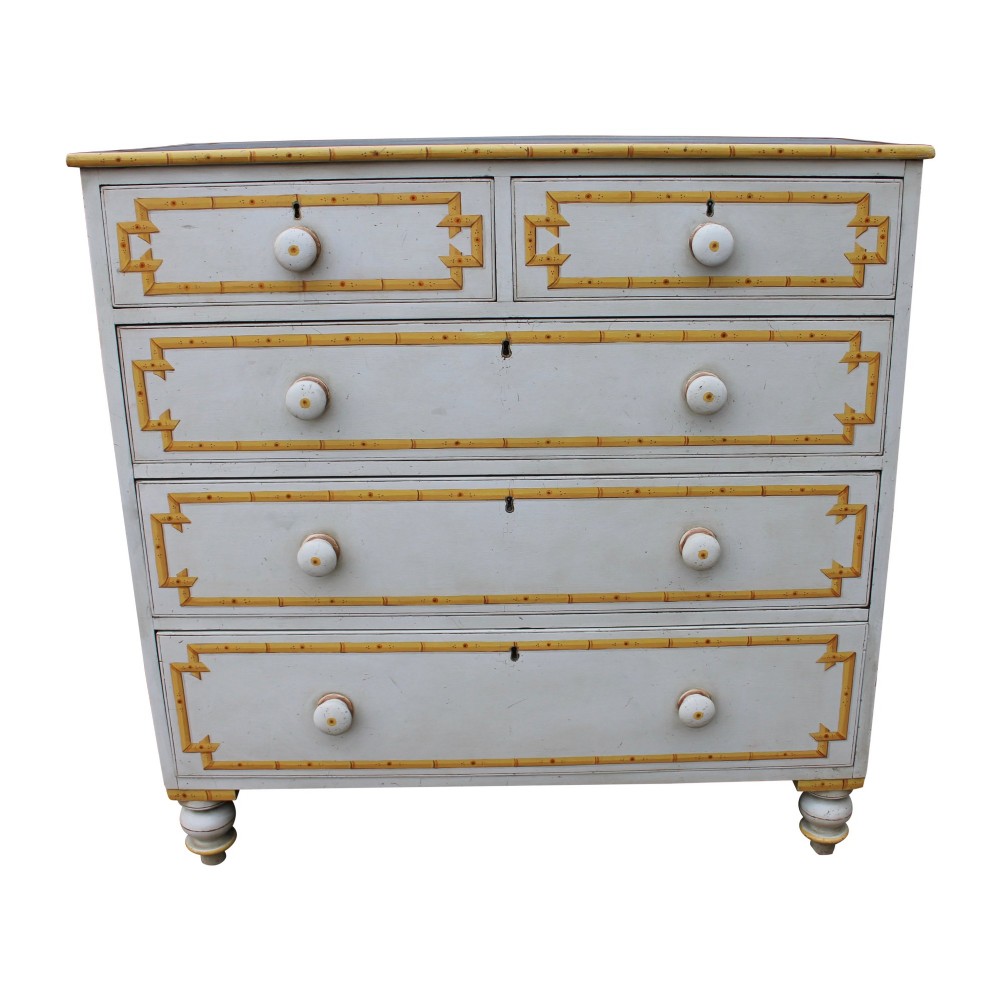 A nineteenth-century off-white painted chest of drawers featuring decorative yellow faux bamboo borders, wooden knobs, and turned feet.