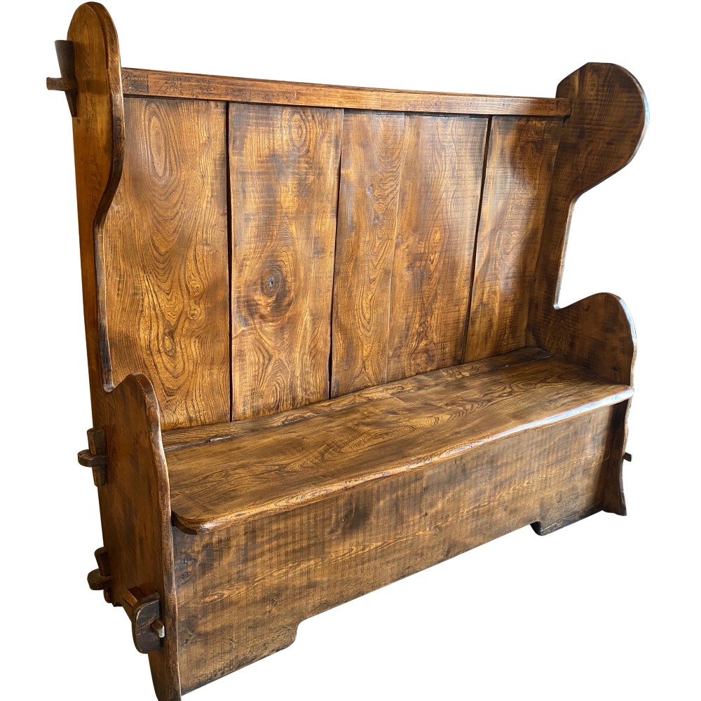 A high-backed 19th-century solid elm box settle with shaped side wings, panelled backrest, and integrated storage seat.