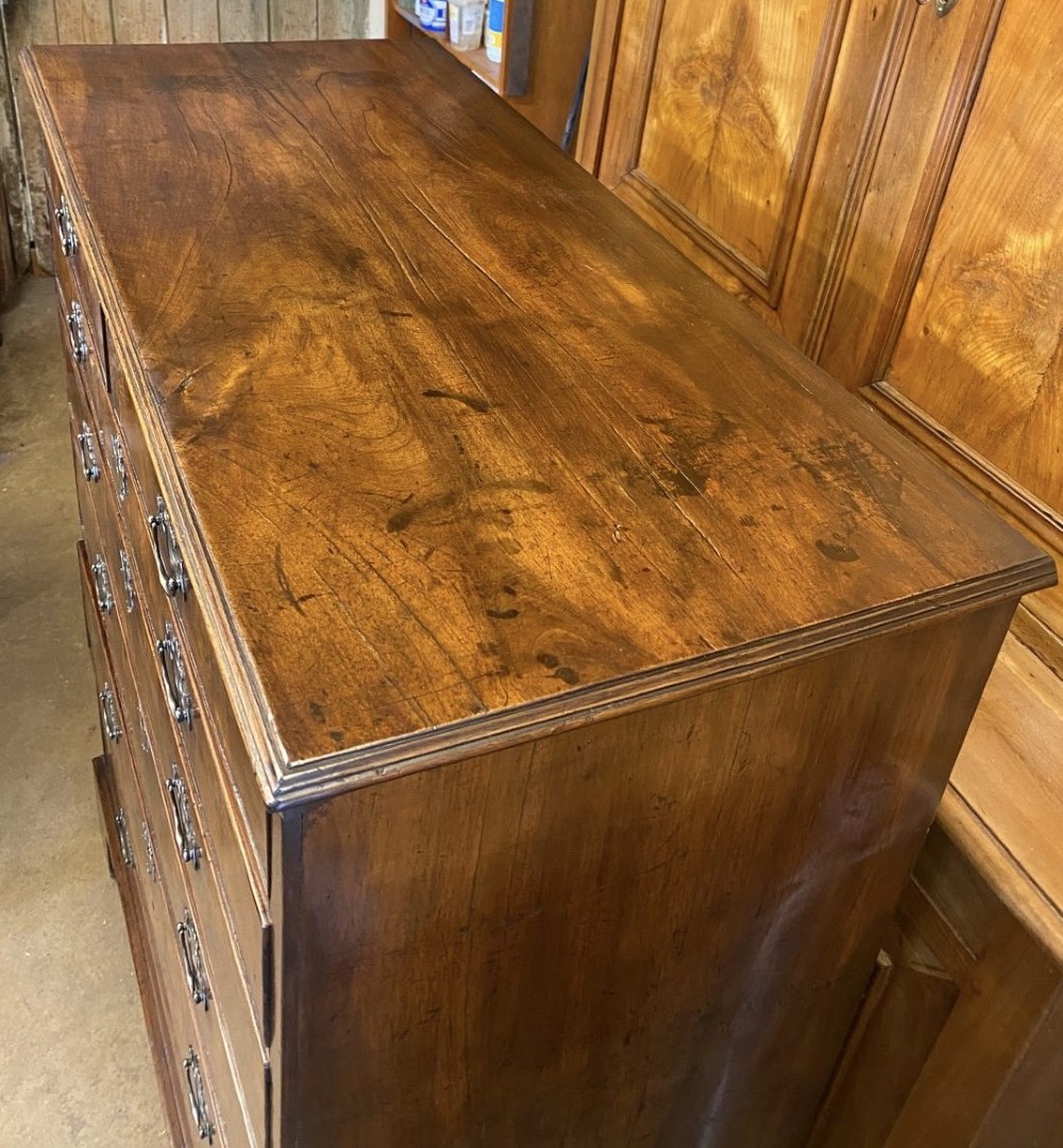 A tall George II walnut chest of drawers featuring figured veneer drawer fronts, brass keyhole escutcheons, brass handles, and bracket feet. View IV