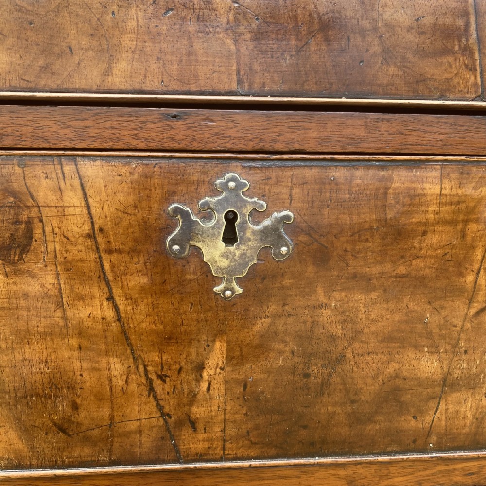 A tall George II walnut chest of drawers featuring figured veneer drawer fronts, brass keyhole escutcheons, brass handles, and bracket feet. View V
