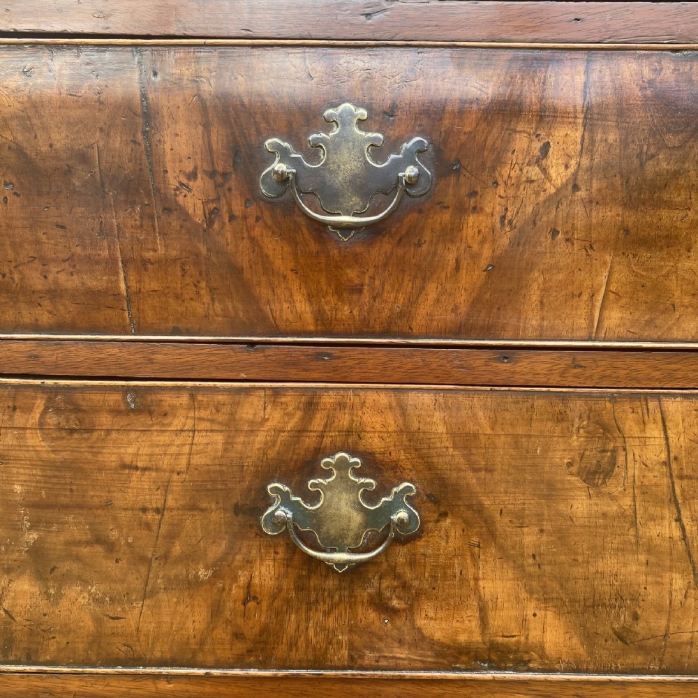 A tall George II walnut chest of drawers featuring figured veneer drawer fronts, brass keyhole escutcheons, brass handles, and bracket feet. View VII