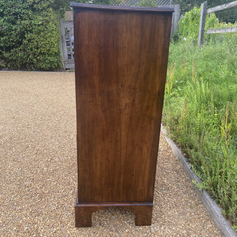 A tall George II walnut chest of drawers featuring figured veneer drawer fronts, brass keyhole escutcheons, brass handles, and bracket feet. View VIII