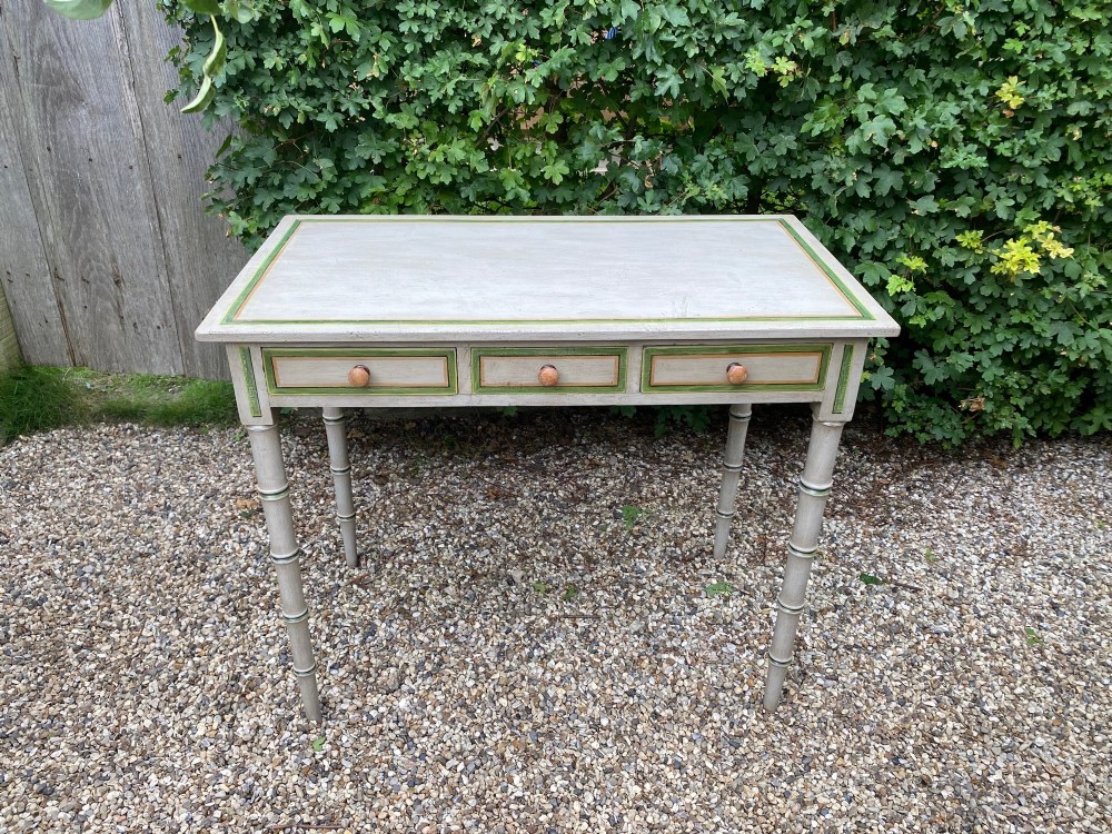 A light grey painted Regency side table featuring green border lining, three drawers with turned wooden knobs, and four legs shaped like bamboo.
