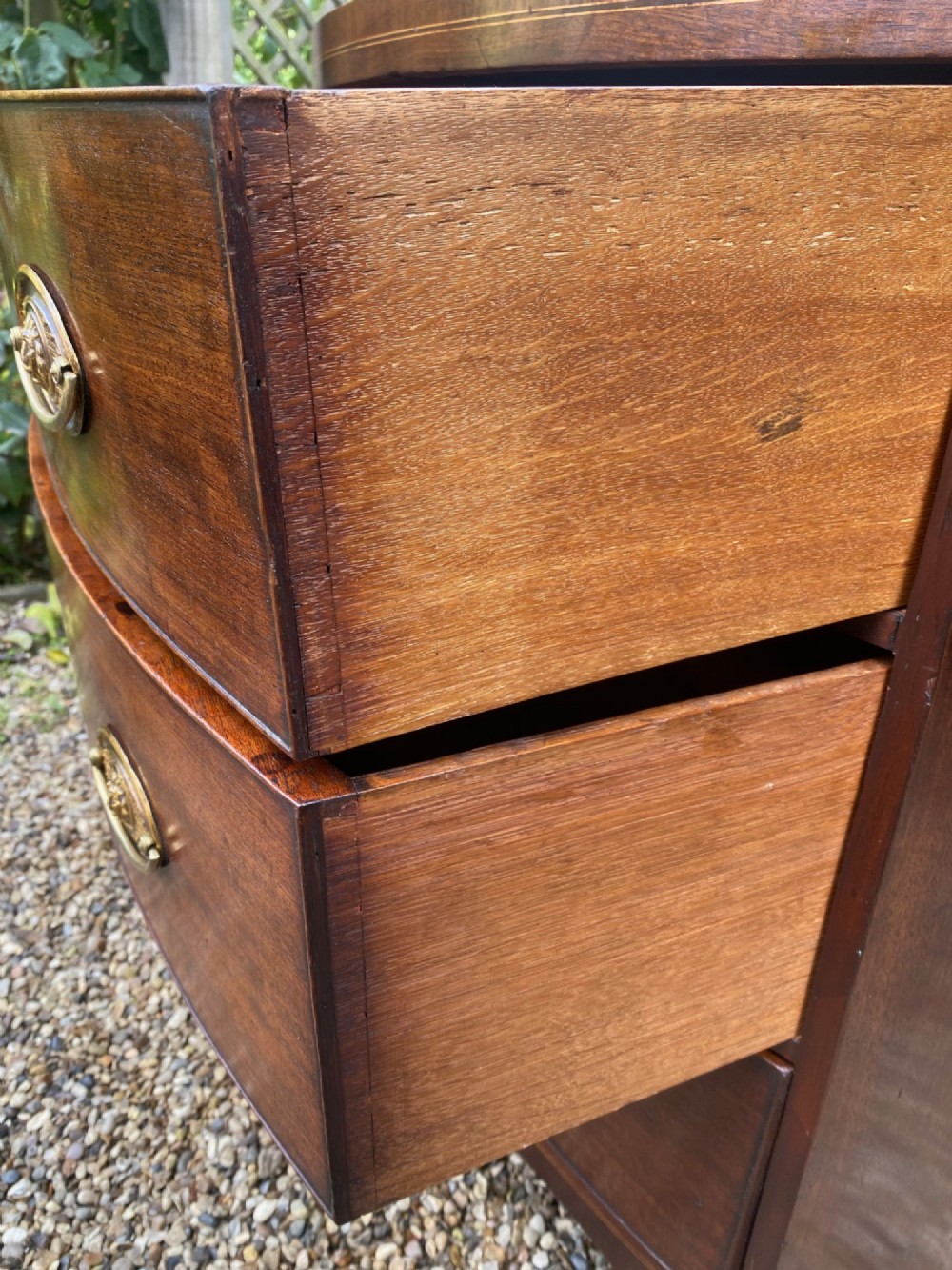 An early nineteenth-century bow-fronted mahogany chest featuring three graduated drawers with brass oval drop handles and a satinwood crossbanded caddy top. View IV