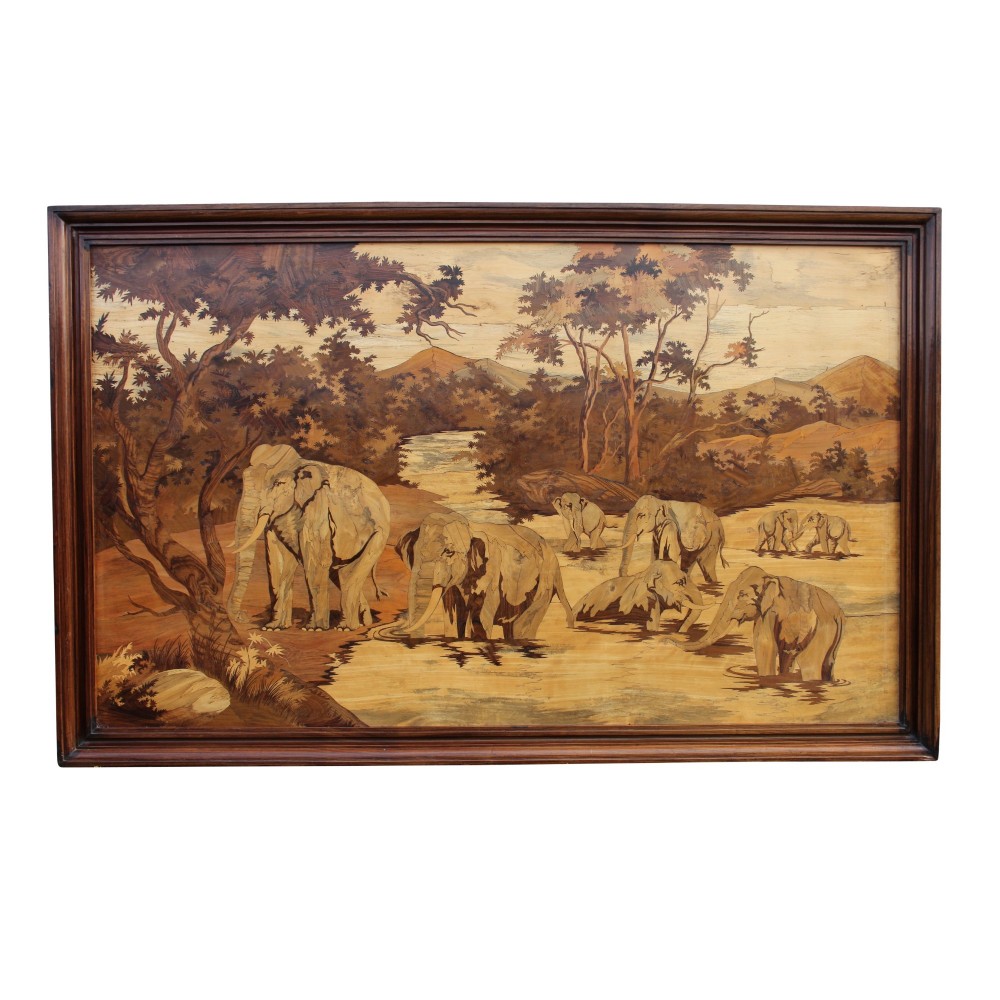 A horizontal framed wooden marquetry panel depicting a herd of elephants bathing in a river surrounded by trees and mountains made from contrasting timber veneers.