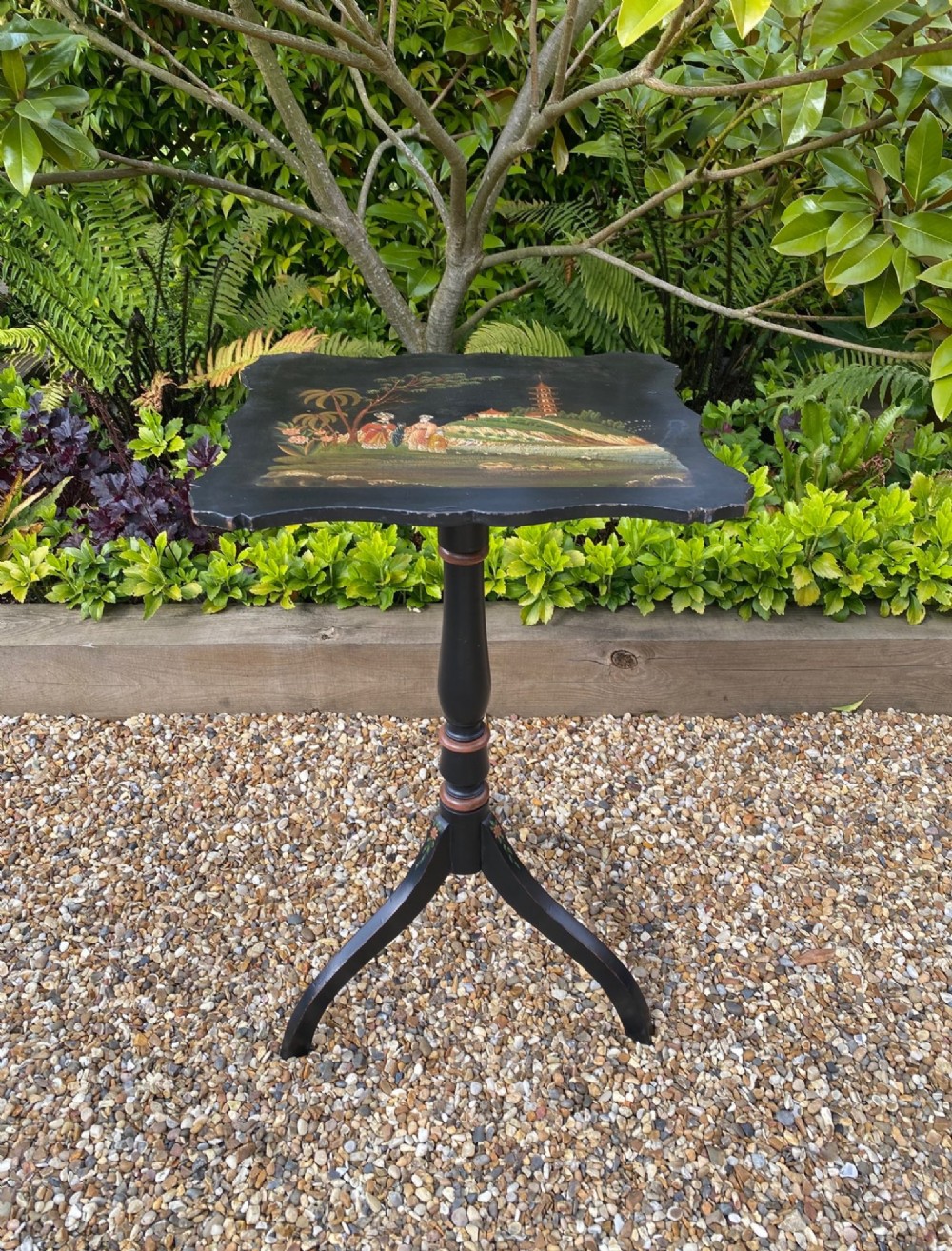A black lacquered tripod side table featuring a shaped top decorated with a hand-painted Chinoiserie landscape scene resting on a turned column pedestal.