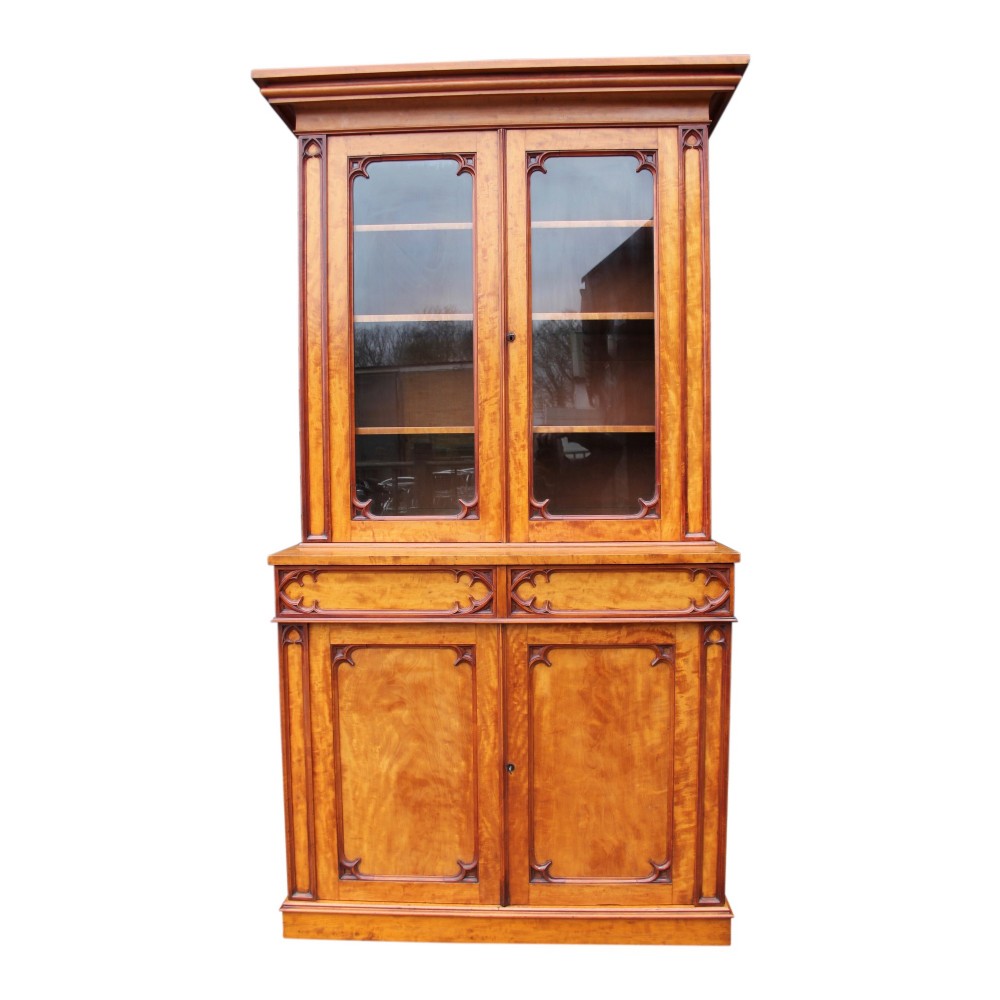 A 19th-century Gothic Revival two-part satinwood bookcase featuring a glazed upper cabinet with tracery trim above a solid door base.