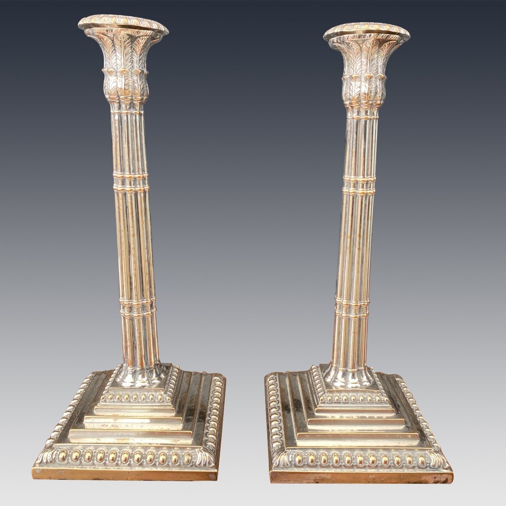 A pair of Georgian silver-plated candlesticks featuring fluted column stems and tiered square bases with beaded borders.