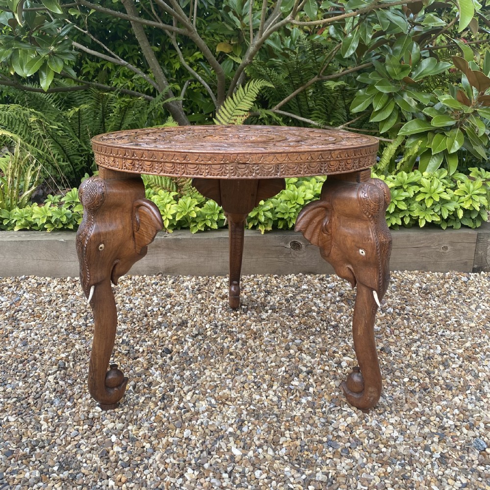 A circular carved rosewood side table supported by three legs shaped as detailed elephant heads with trunks extending to the floor.