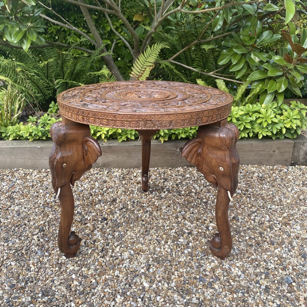 A circular carved rosewood side table supported by three legs shaped as detailed elephant heads with trunks extending to the floor. View II