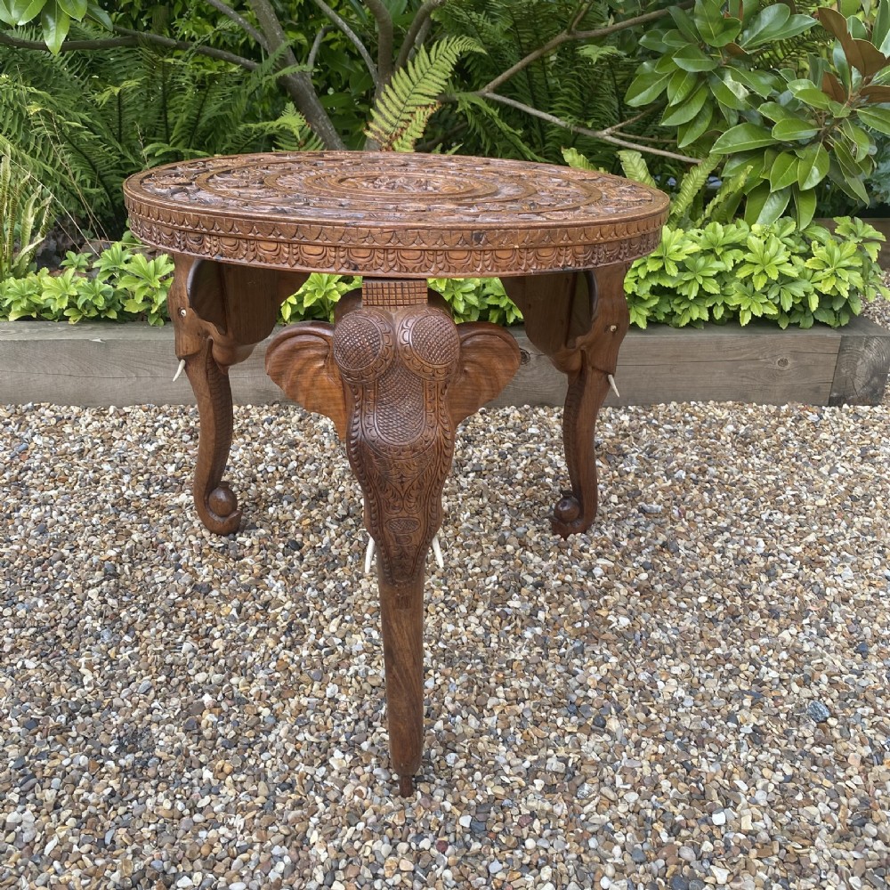 A circular carved rosewood side table supported by three legs shaped as detailed elephant heads with trunks extending to the floor. View VI