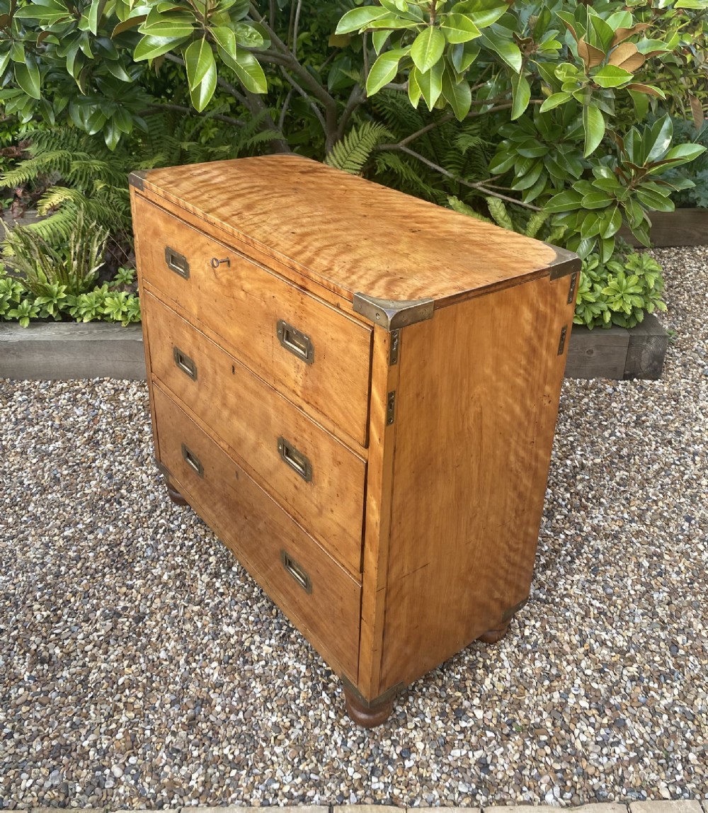 A mid-19th-century satin birch military campaign chest featuring three full-width drawers with flush recessed brass handles and corner brass protective brackets. View II