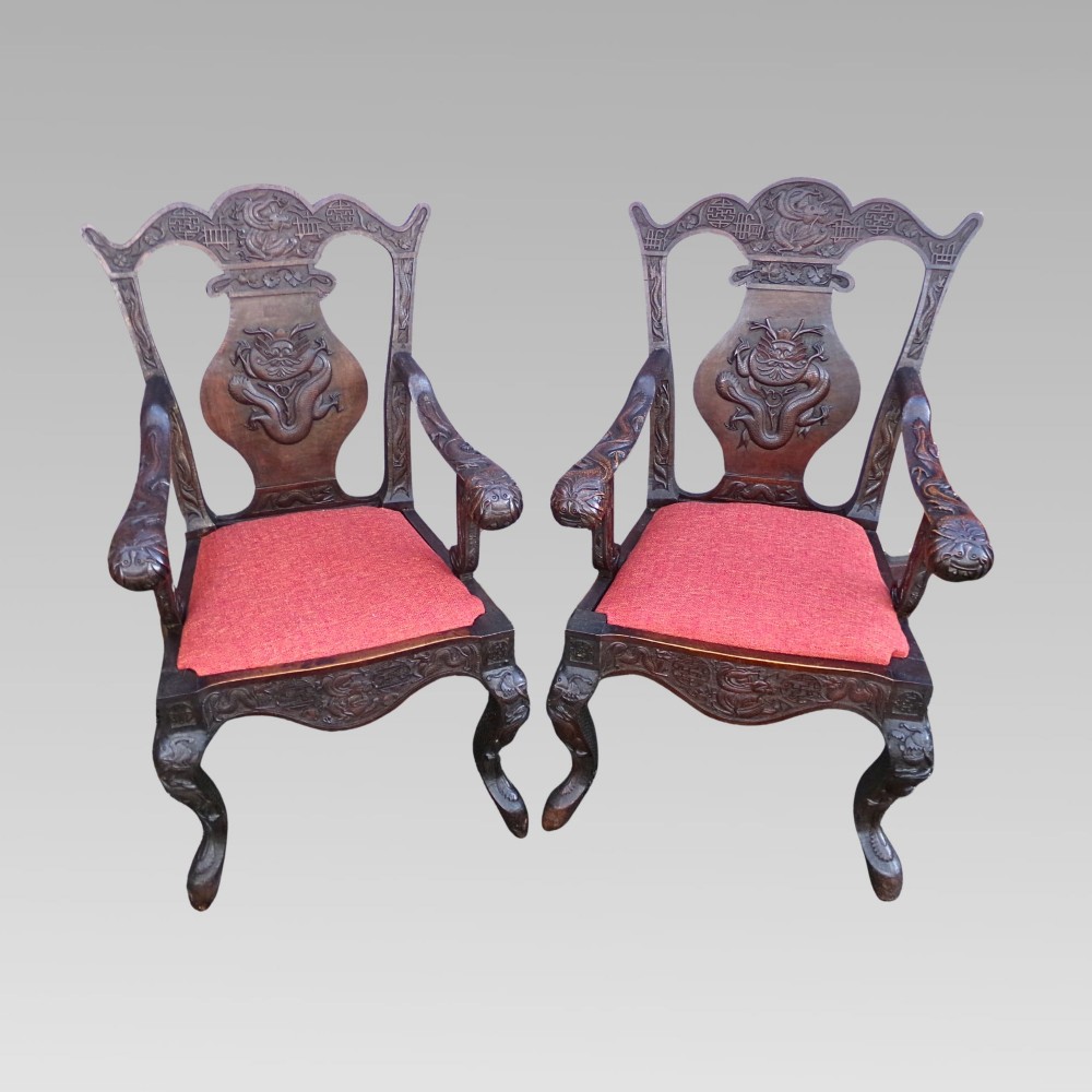 A pair of dark carved hardwood armchairs featuring high back splats with dragon relief motifs, dragon head terminal arms, and red upholstered seats. View II