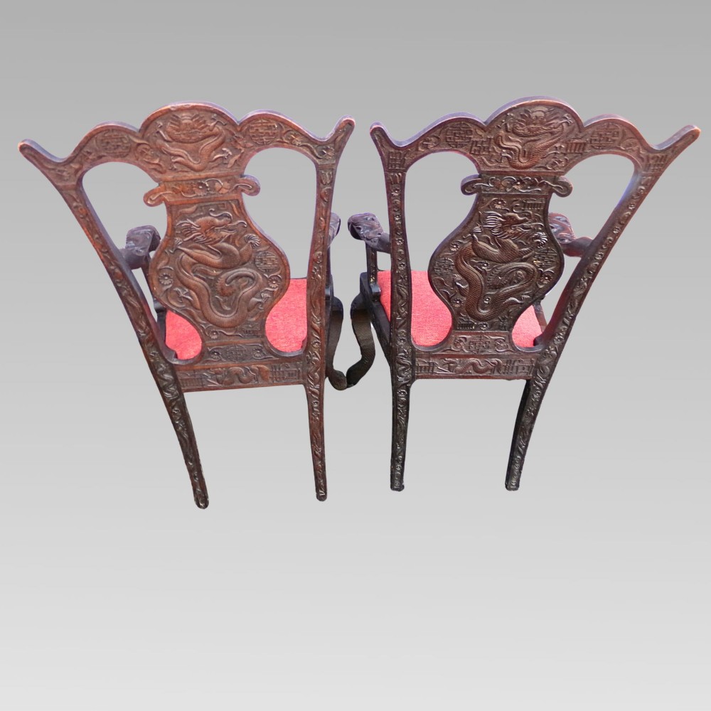 A pair of dark carved hardwood armchairs featuring high back splats with dragon relief motifs, dragon head terminal arms, and red upholstered seats. View III