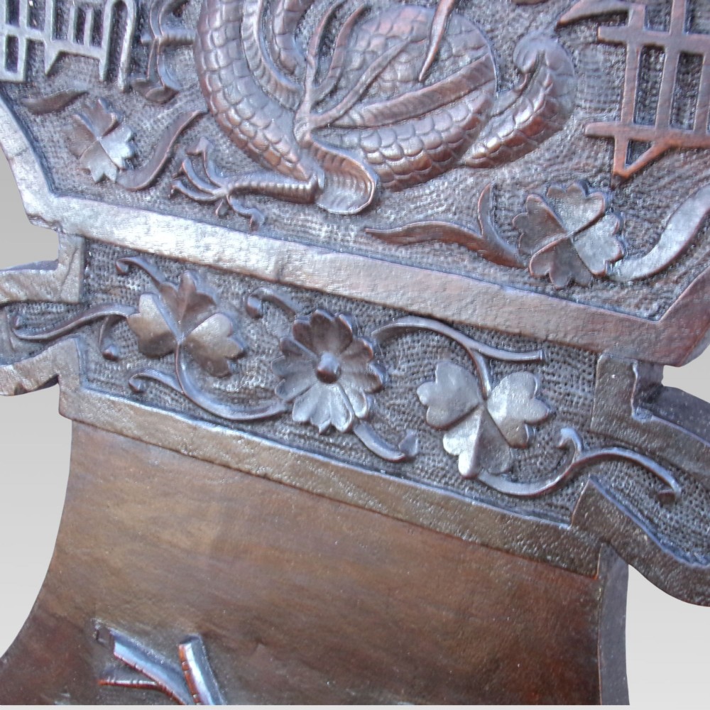 A pair of dark carved hardwood armchairs featuring high back splats with dragon relief motifs, dragon head terminal arms, and red upholstered seats. View VI