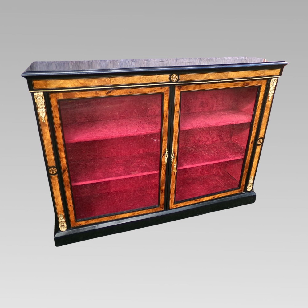A 19th-century Victorian walnut and ebonised display cabinet featuring two glazed doors, gilt metal mounts, and a magenta velvet interior. View II