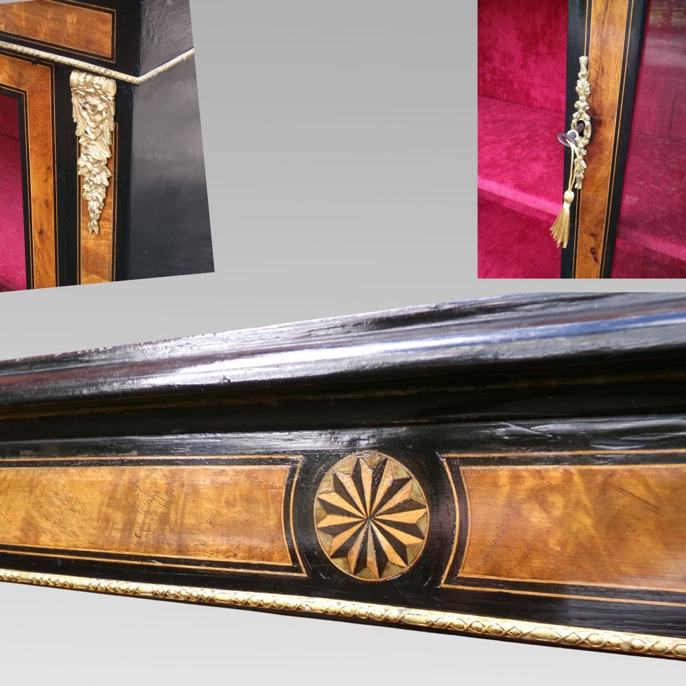 A 19th-century Victorian walnut and ebonised display cabinet featuring two glazed doors, gilt metal mounts, and a magenta velvet interior. View V