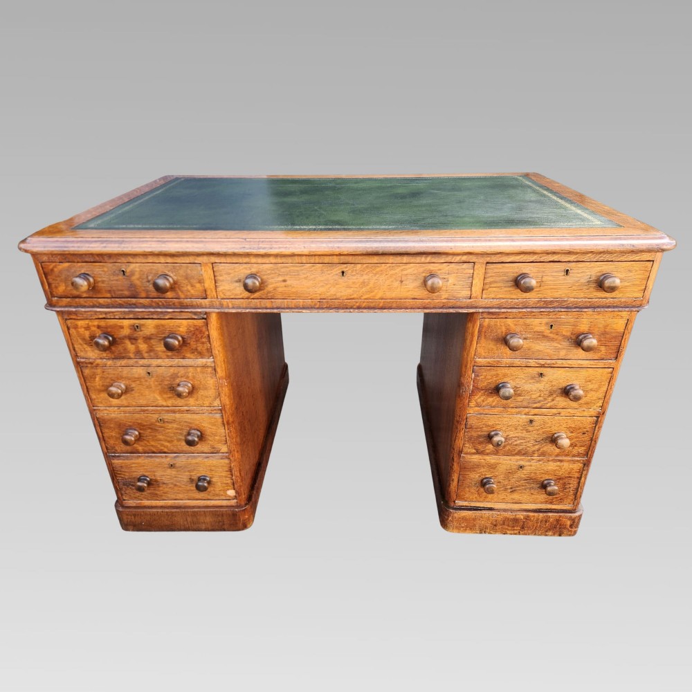 A Victorian oak pedestal writing desk featuring a green leather inset top and multiple drawers with turned wooden handles.