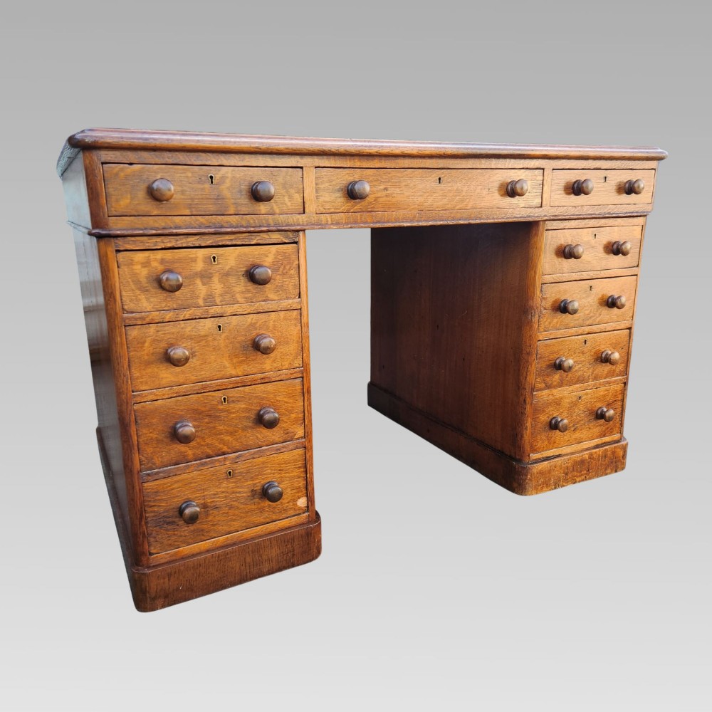 A Victorian oak pedestal writing desk featuring a green leather inset top and multiple drawers with turned wooden handles. View II