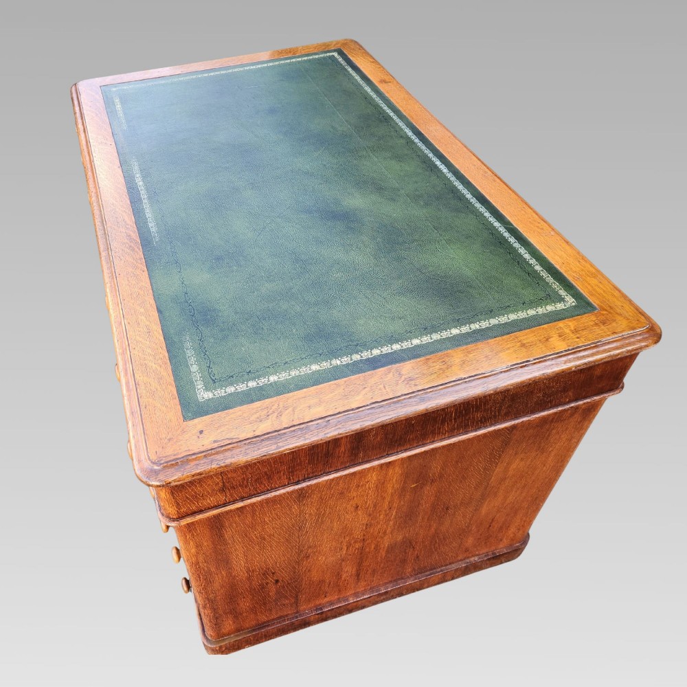 A Victorian oak pedestal writing desk featuring a green leather inset top and multiple drawers with turned wooden handles. View III