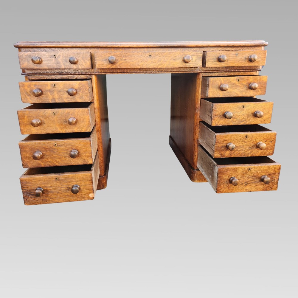 A Victorian oak pedestal writing desk featuring a green leather inset top and multiple drawers with turned wooden handles. View V