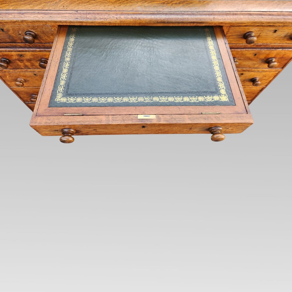 A Victorian oak pedestal writing desk featuring a green leather inset top and multiple drawers with turned wooden handles. View VII