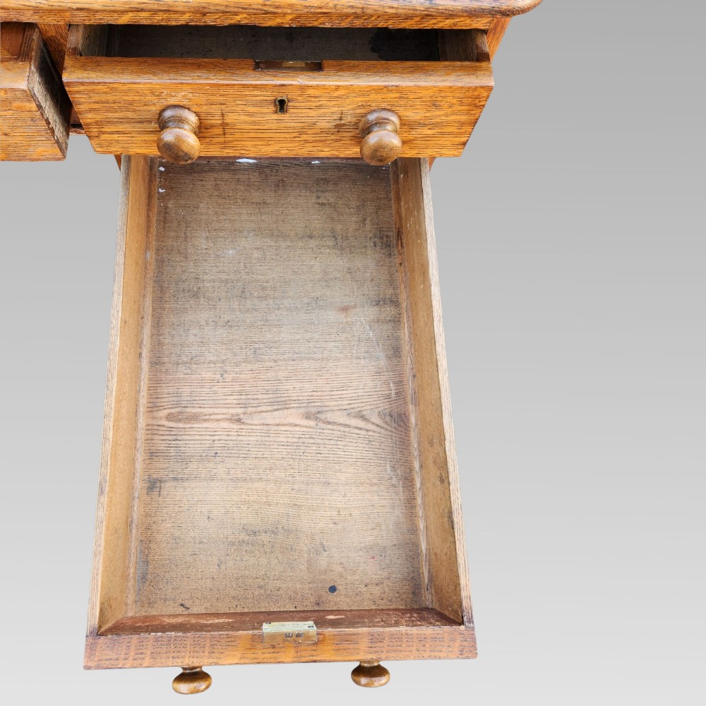 A Victorian oak pedestal writing desk featuring a green leather inset top and multiple drawers with turned wooden handles. View VIII