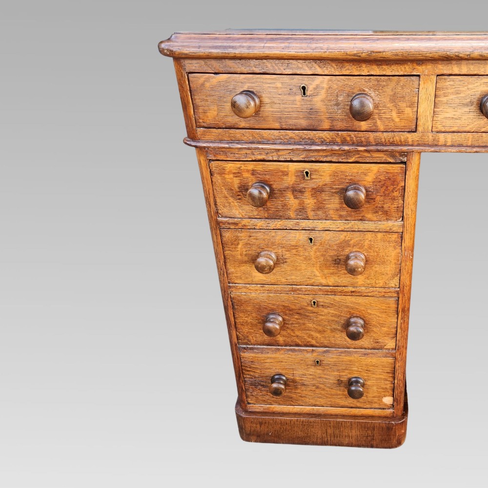 A Victorian oak pedestal writing desk featuring a green leather inset top and multiple drawers with turned wooden handles. View IX