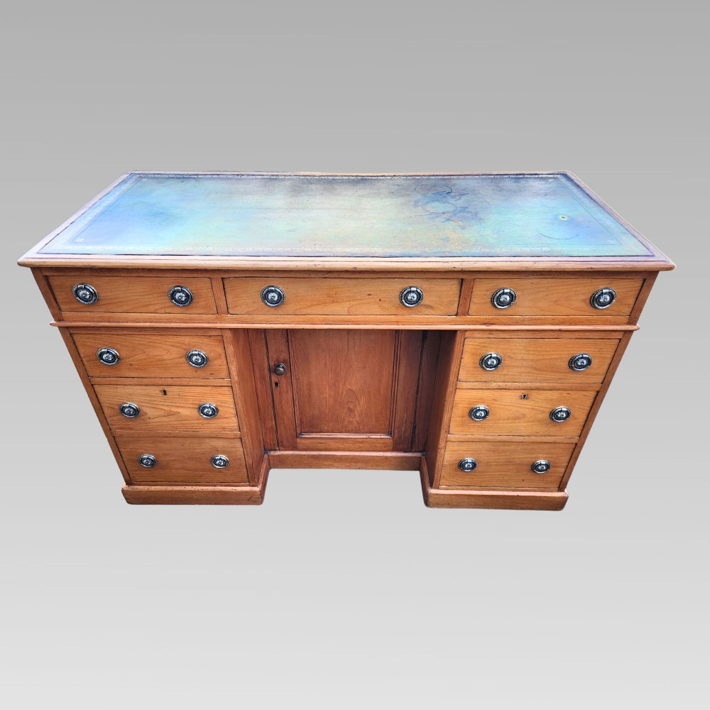 An antique Victorian pine pedestal writing desk featuring a green leather inset top and twin pedestals fitted with drawers and brass ring handles.
