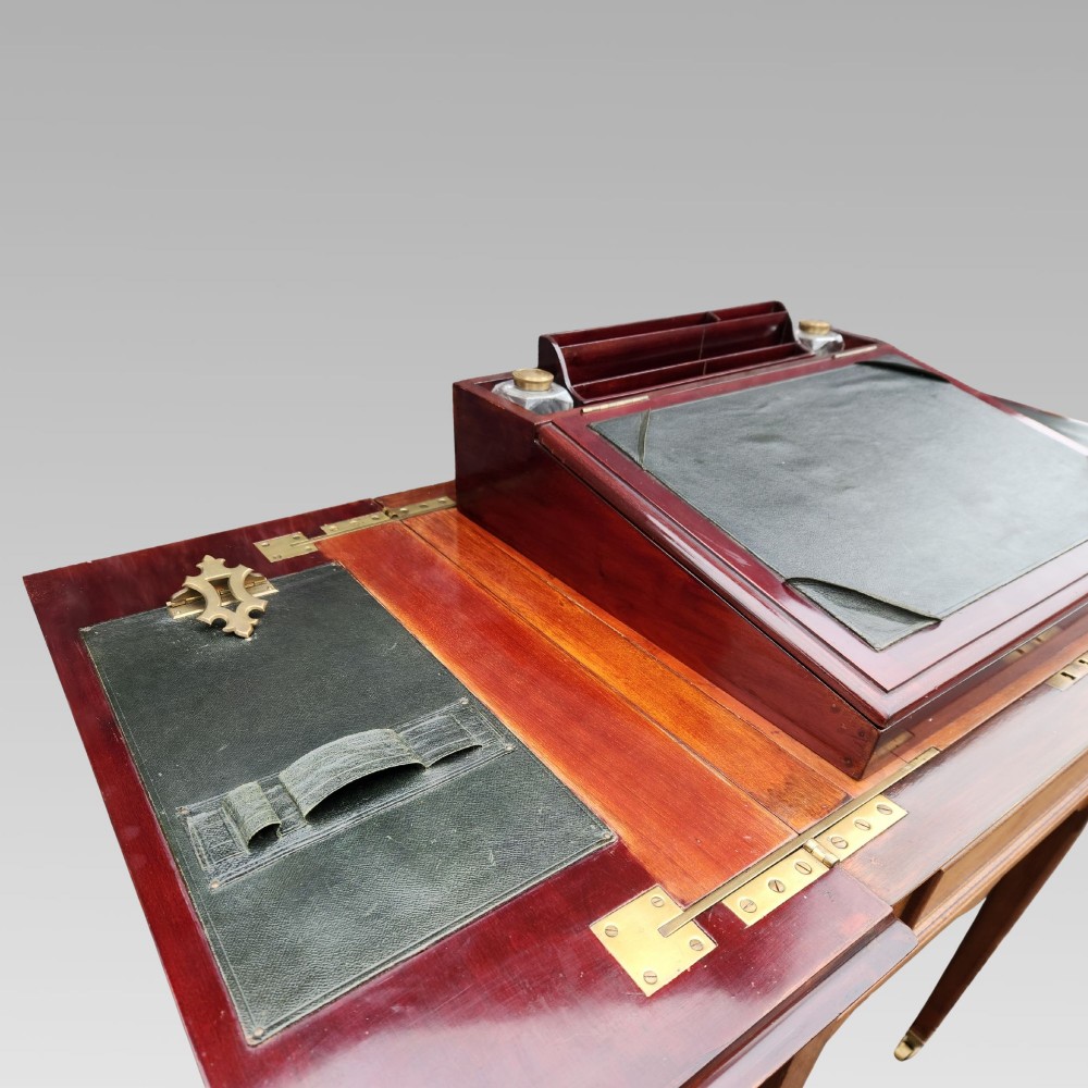 An open antique Edwardian mahogany metamorphic writing desk featuring fold-out side flaps, a green leather writing surface, integrated inkwells, and brass fittings. View VII