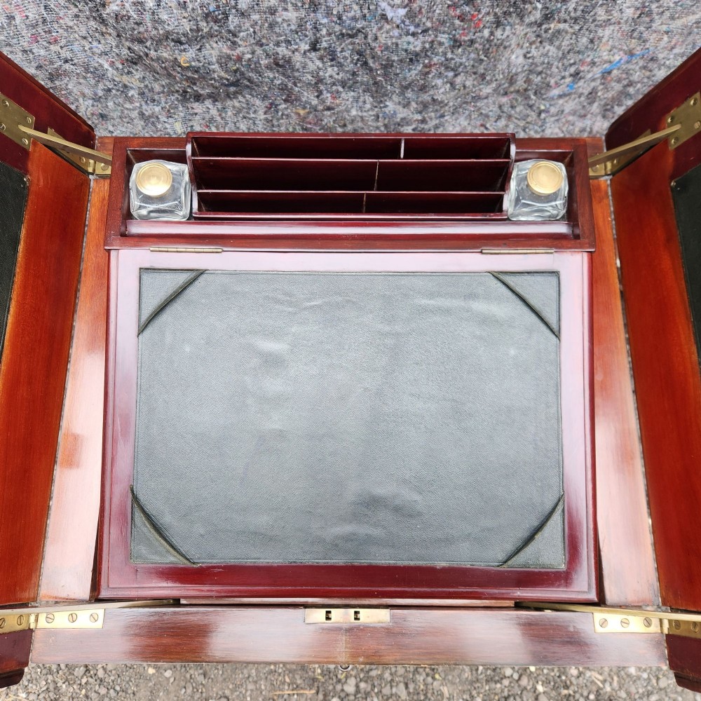 An open antique Edwardian mahogany metamorphic writing desk featuring fold-out side flaps, a green leather writing surface, integrated inkwells, and brass fittings. View X