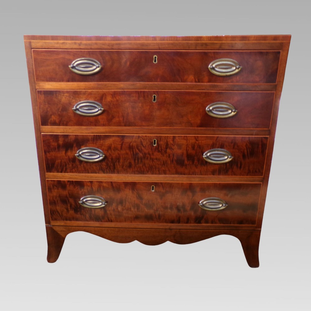 A George III style mahogany chest of four drawers featuring flame mahogany drawer fronts, satinwood line inlay, brass oval handles, and bracket feet. View II