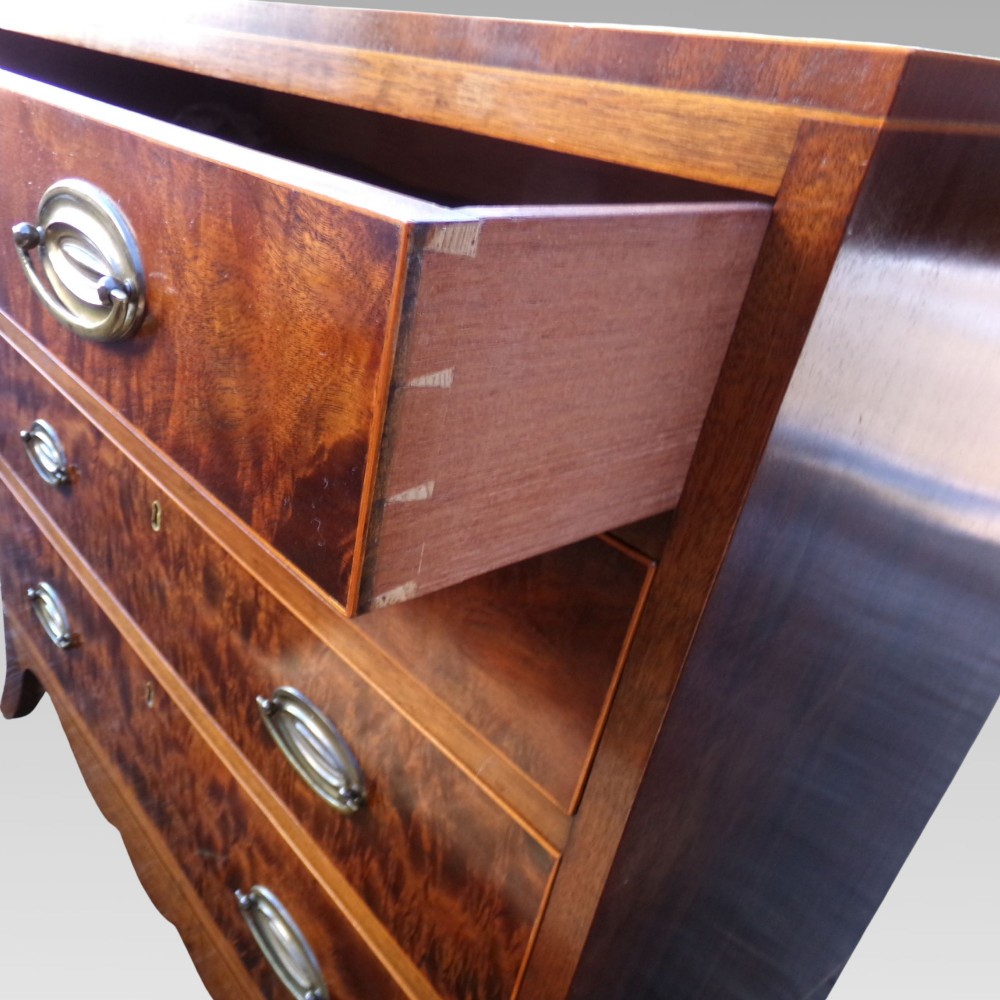 A George III style mahogany chest of four drawers featuring flame mahogany drawer fronts, satinwood line inlay, brass oval handles, and bracket feet. View VI