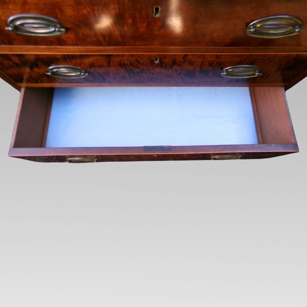 A George III style mahogany chest of four drawers featuring flame mahogany drawer fronts, satinwood line inlay, brass oval handles, and bracket feet. View VII