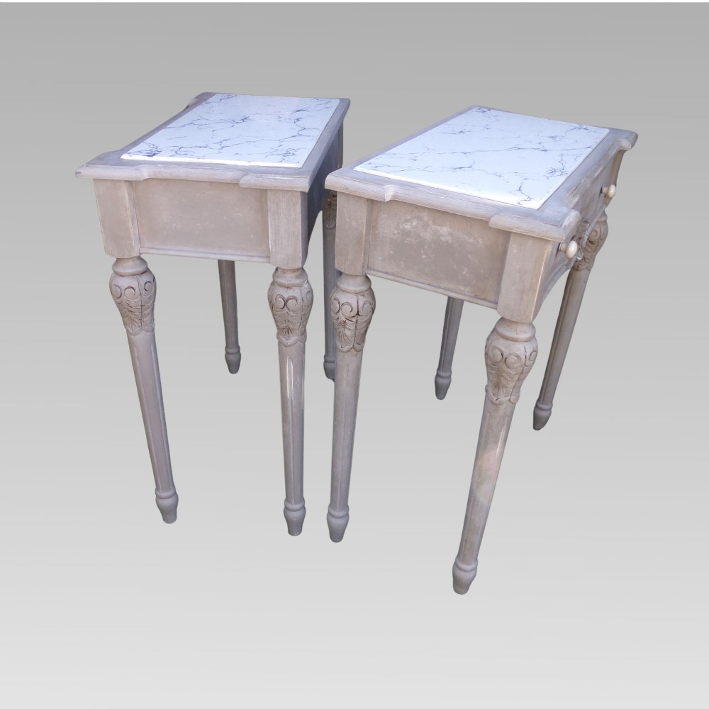 A pair of distressed grey painted French bedside tables featuring white marble inset tops and carved wooden legs. View V