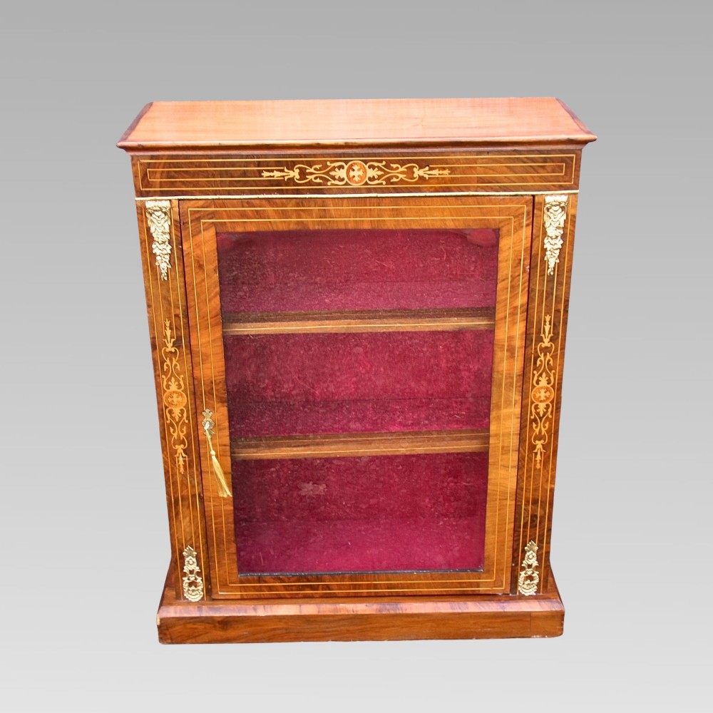 A nineteenth-century walnut veneer pier cabinet featuring floral marquetry inlay, gilt brass mounts, a single glazed door, and a red velvet lined interior.