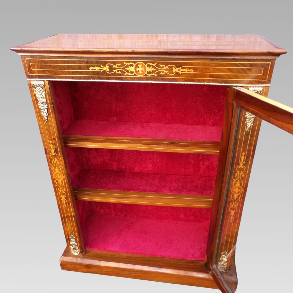 A nineteenth-century walnut veneer pier cabinet featuring floral marquetry inlay, gilt brass mounts, a single glazed door, and a red velvet lined interior. View V
