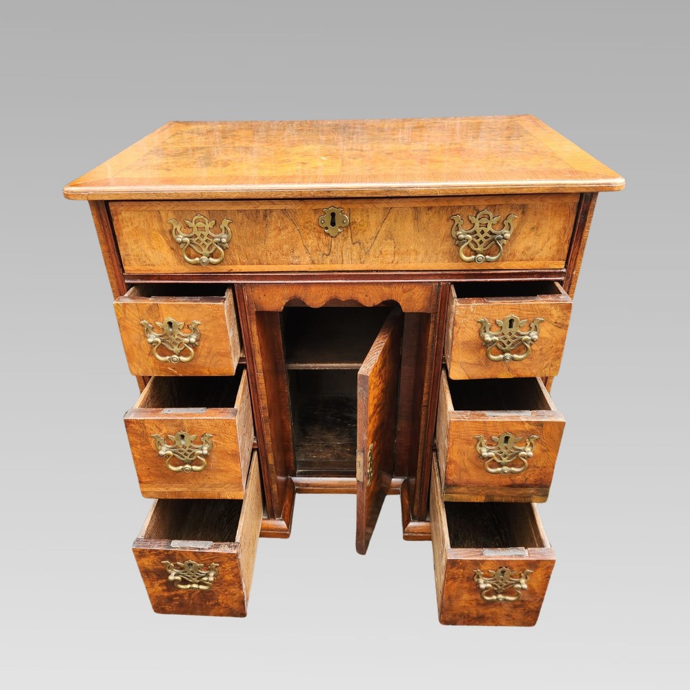 An antique Queen Anne style burr walnut kneehole desk featuring a crossbanded top, brass drop handles, a central recessed cupboard, and bracket feet. View II