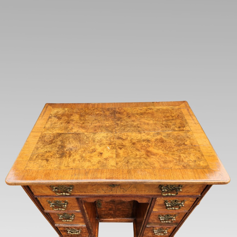 An antique Queen Anne style burr walnut kneehole desk featuring a crossbanded top, brass drop handles, a central recessed cupboard, and bracket feet. View III