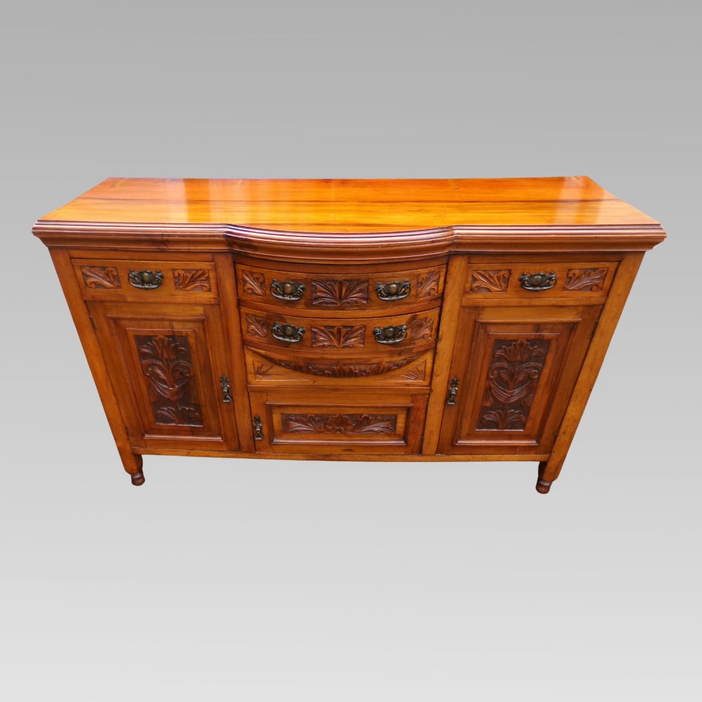 A carved Edwardian mahogany sideboard featuring a bow-front centre section with drawers, flanked by cupboard doors with stylised plant motifs.