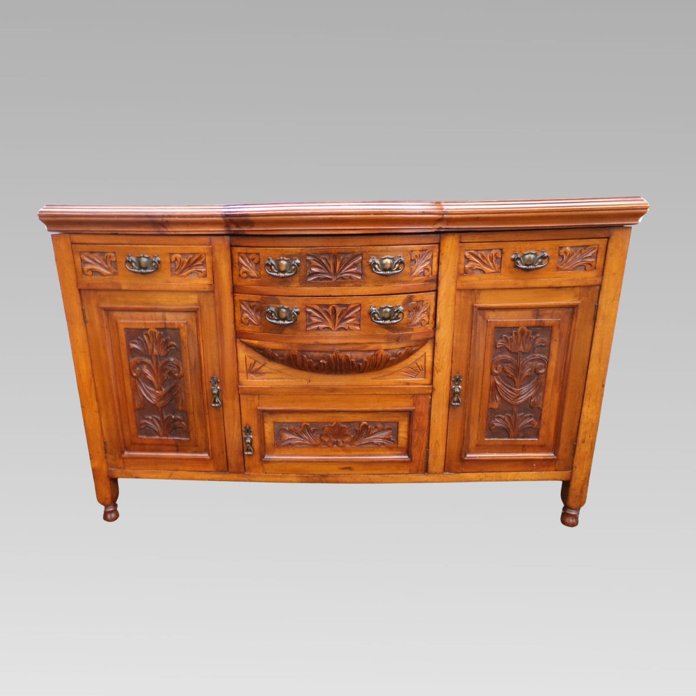 A carved Edwardian mahogany sideboard featuring a bow-front centre section with drawers, flanked by cupboard doors with stylised plant motifs. View II