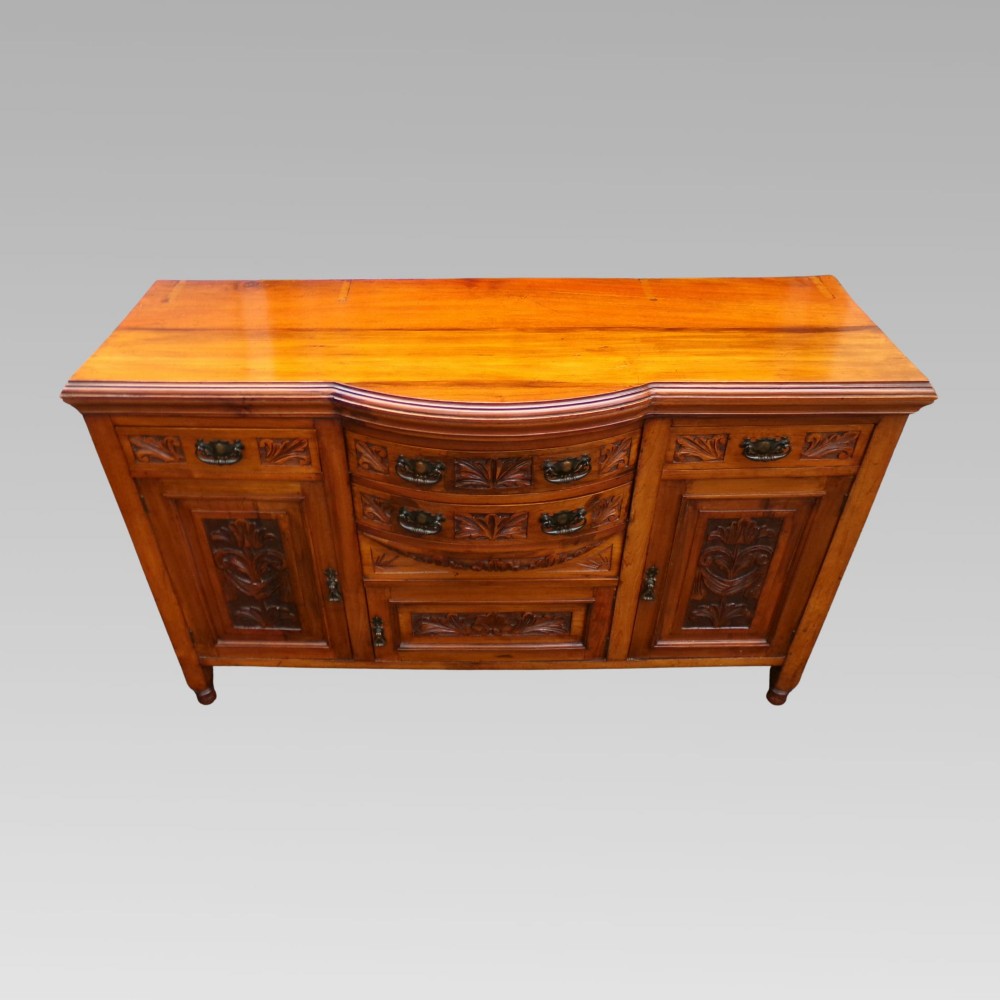 A carved Edwardian mahogany sideboard featuring a bow-front centre section with drawers, flanked by cupboard doors with stylised plant motifs. View III